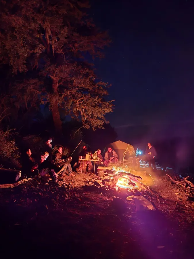 Socios del club sentados alrededor de la fogata de noche, junto a las carpas del campamento