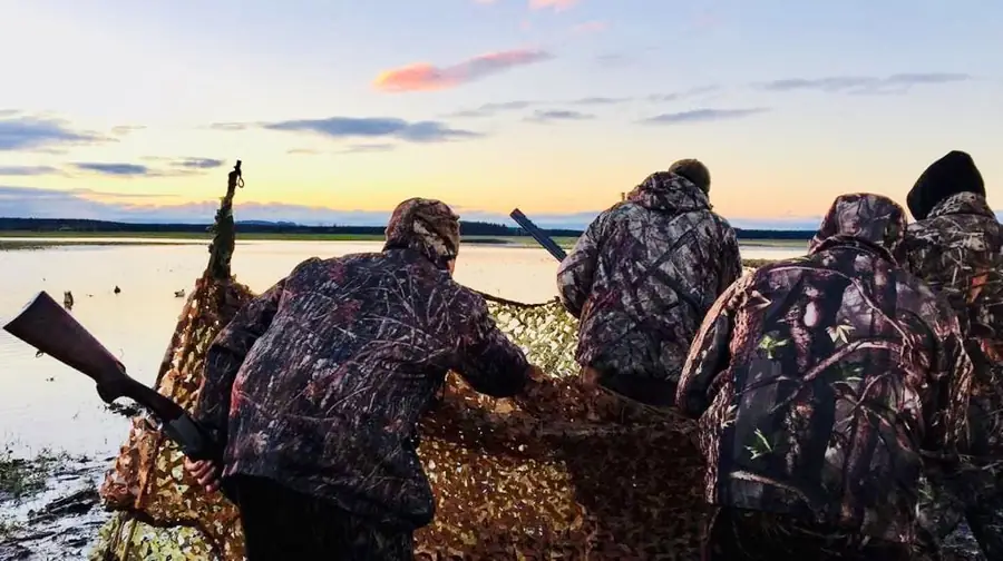 Cazadores de espaldas en la orilla, contra el cielo del atardecer