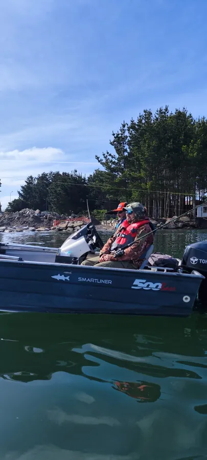 Dos socios pescando desde el bote a motor, con la costa arbolada al fondo