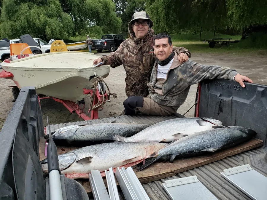 Dos socios del club arrodillados junto a cuatro salmones chinook sobre la camioneta
